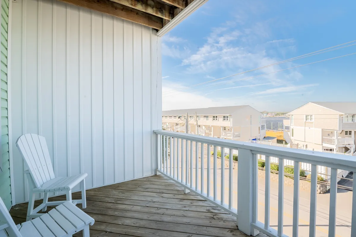 A peaceful wooden deck with white Adirondack chairs offers views of nearby buildings and the blue sky. The setting is tranquil, ideal for unwinding after a day outside, perhaps with a pet at your feet.