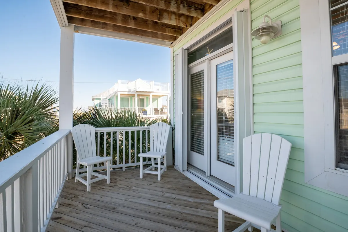 An inviting wooden deck featuring classic white Adirondack chairs set against a green exterior wall, hinting at a peaceful outdoor living space. The setup invites guests to unwind, enjoy the view, and take in the fresh air, with the suggestion of a scenic backdrop beyond the deck.