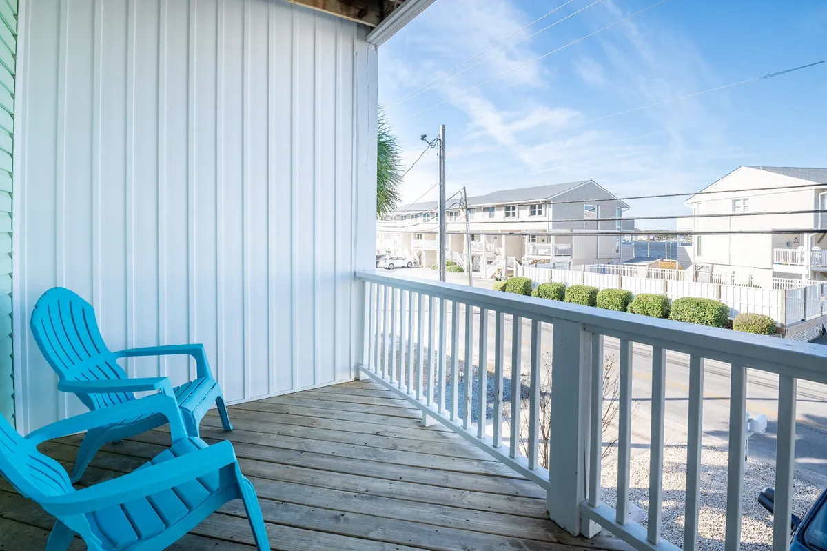 A charming outdoor deck with a vibrant blue Adirondack chair, wooden planks underfoot, and lush greenery along the edges. The setting invites you to sit and enjoy the sunrise, feel the salty breeze, or unwind after a day of adventure.