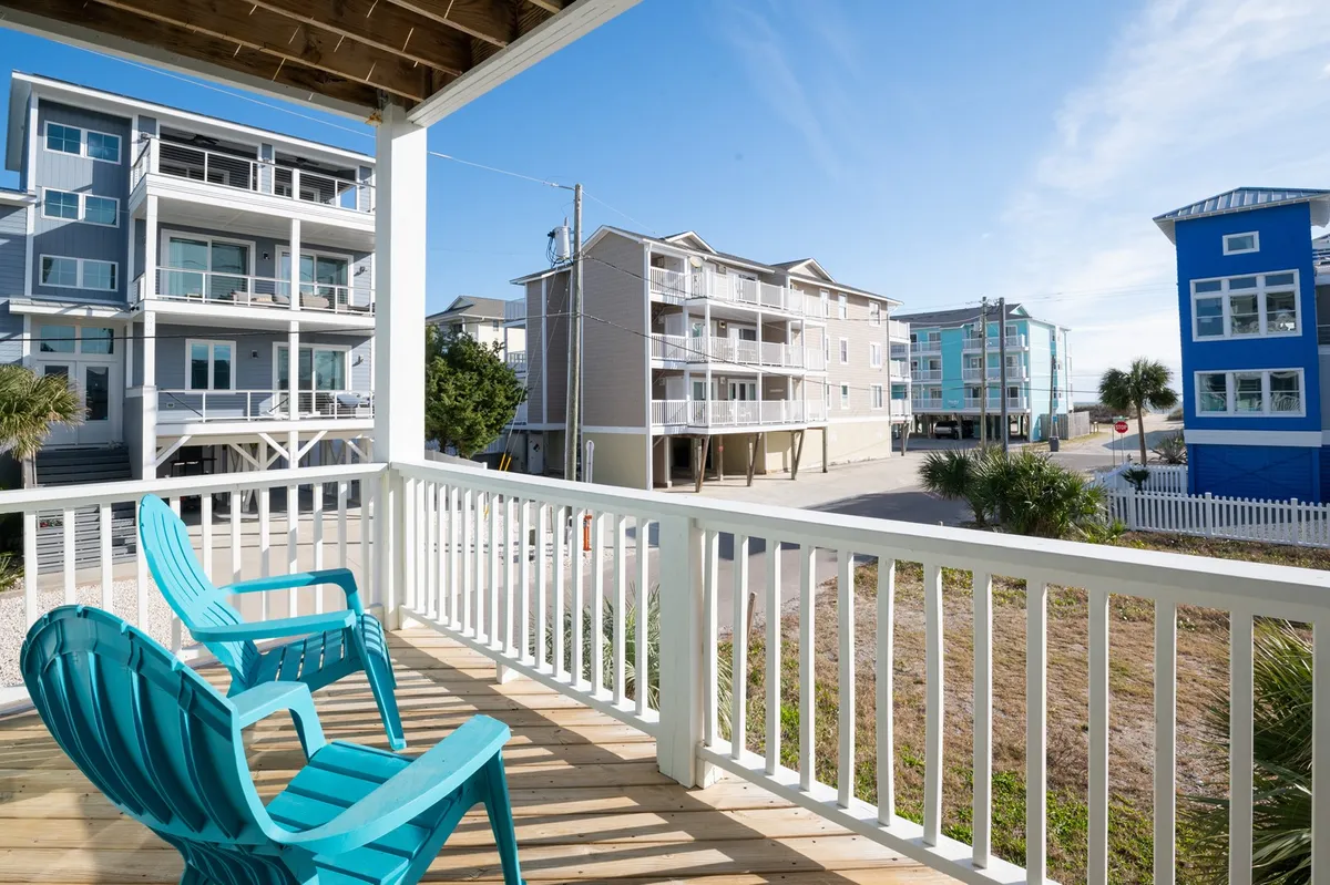 Turquoise chairs on a balcony look out over the landscape, with palm trees and nearby buildings visible in the background. The setup invites families to relax, sip coffee, and enjoy the coastal breeze while keeping an eye on the action below.