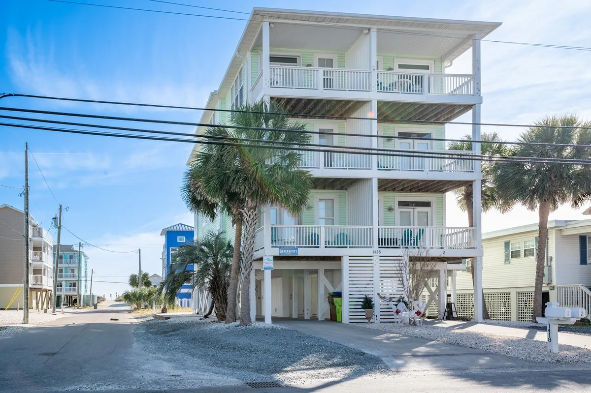 An exterior view of the three-story building with covered parking, palm trees, balconies, and welcoming front steps. The scene is sunlit and inviting, emphasizing accessibility and ease of arrival.