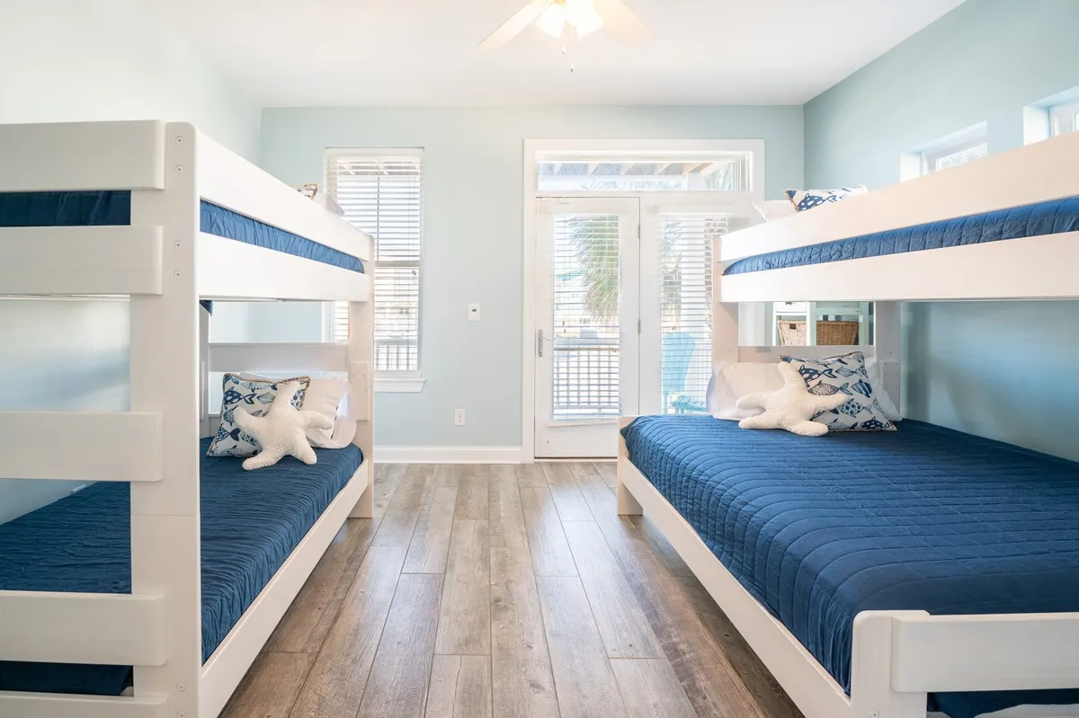 A playful bunk room with bright bunk beds, large windows spilling in sunlight, and cheerful decorative pillows. The space feels inviting and fun, perfect for kids or cousins to read, play, and make vacation memories together.