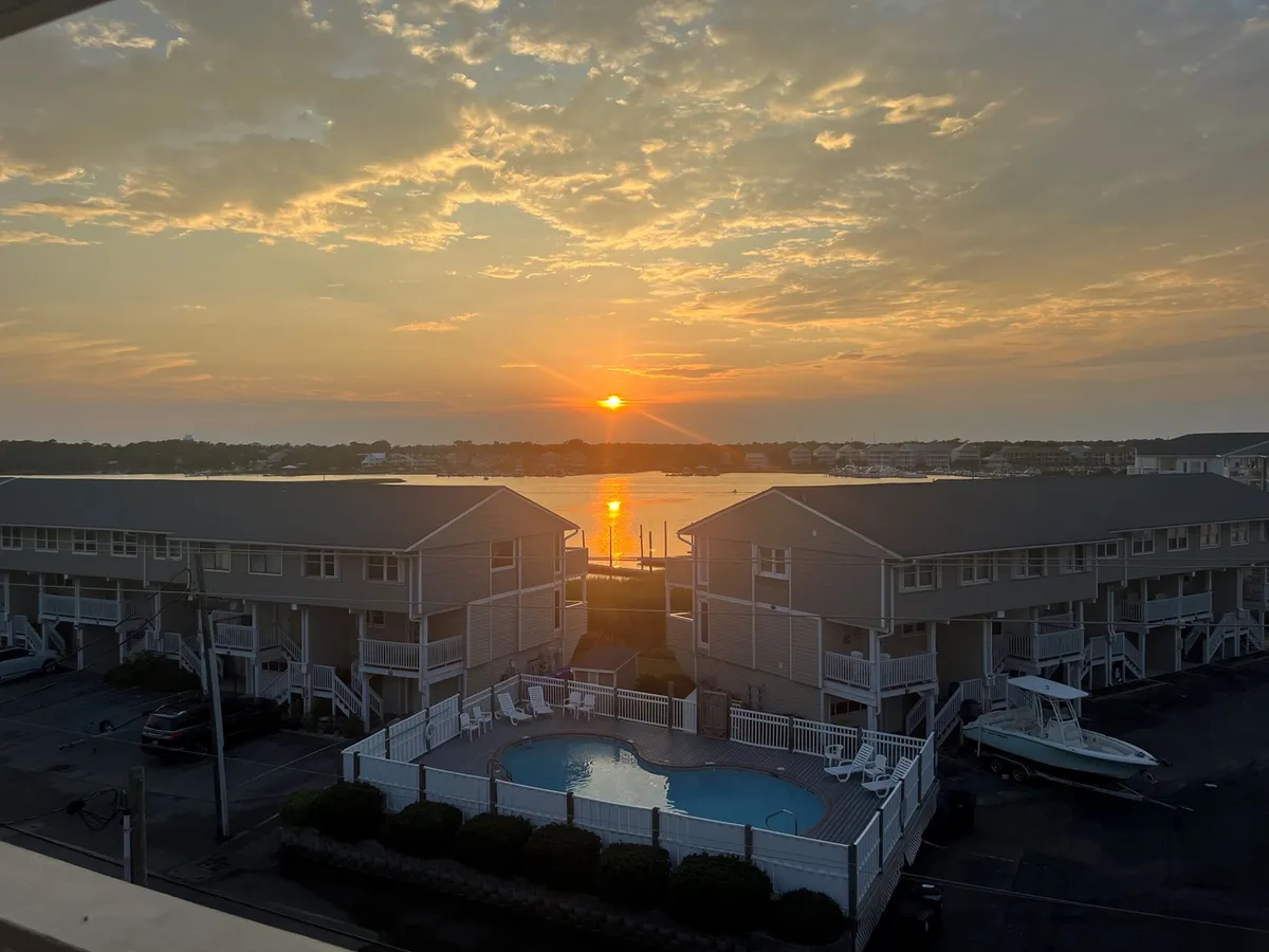 A stunning view at sunset, with the sun reflecting off the water, boats docked nearby, a swimming pool in the foreground, and buildings lining the waterfront. The scene embodies relaxation, adventure, and a sense of place by the water.