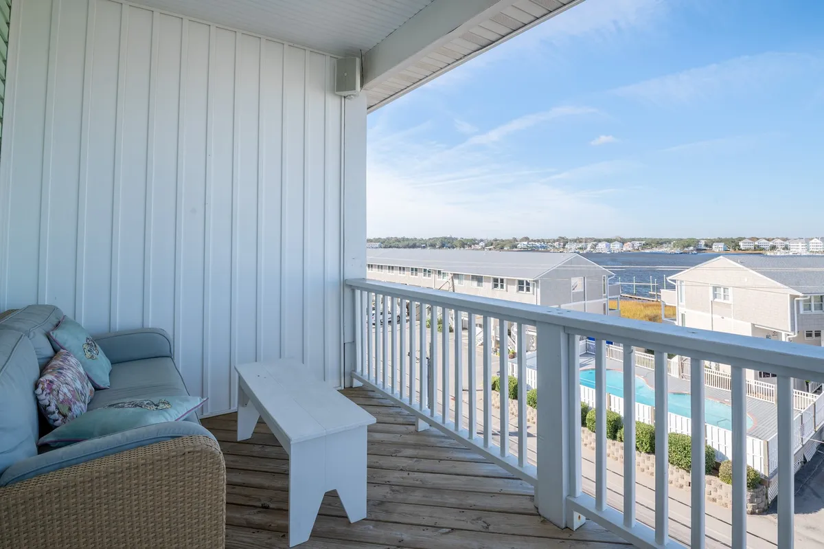 A serene exterior balcony setup with comfortable seating overlooking a pool and a view of the water. The scene captures tranquil moments perfect for sipping coffee, reading, or watching boats go by, with the calming blue of the pool and water in the background.